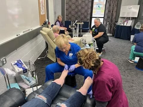 Two nurses giving foot care to a patient in a training room