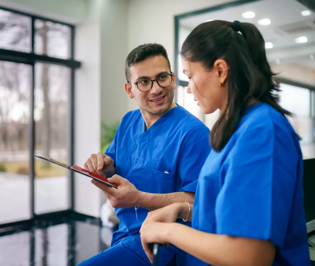 Two nurses in blue scrubs reviewing information on a tablet