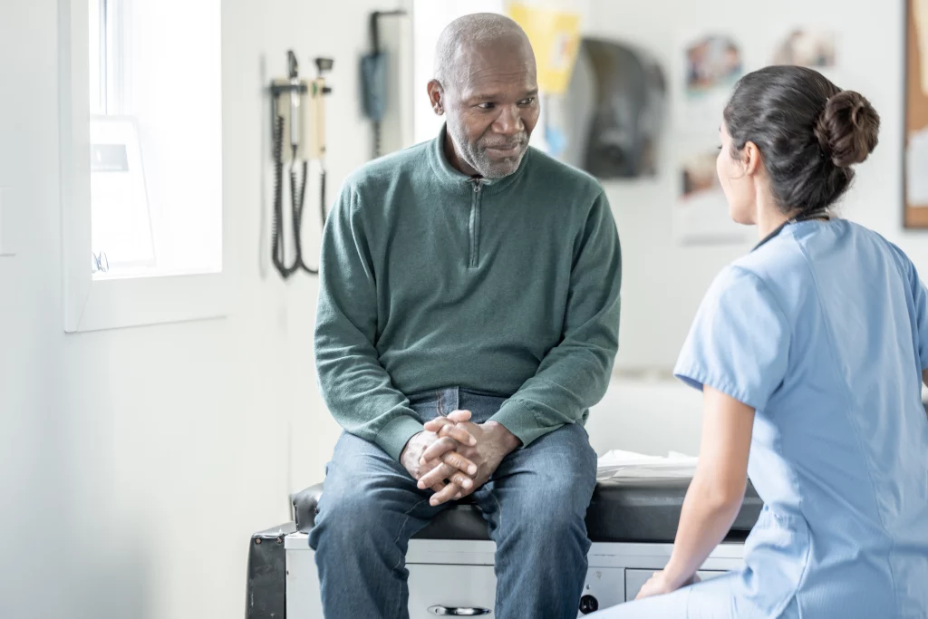 Nurse in light blue scrubs talking with a male patient seated on an exam table