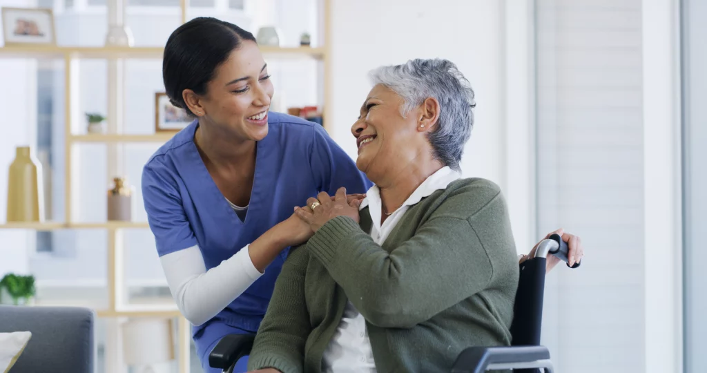 Smiling nurse holding the hands of an older woman in a wheelchair